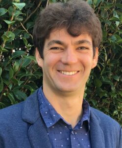 A man smiling in front of a bush.